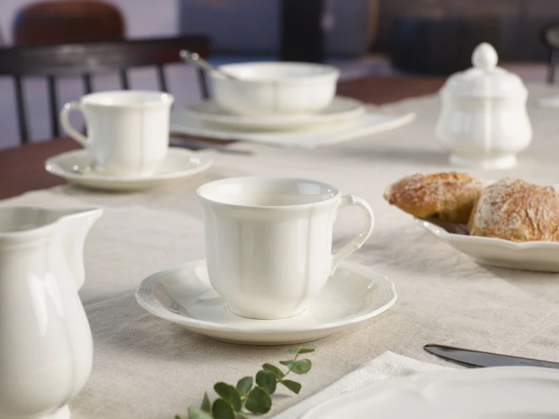 manoir-coffee-tea-table-setting A serene breakfast table with white ceramic cups, saucers, and a sugar bowl on a light tablecloth. Fresh pastries add a warm, inviting touch.