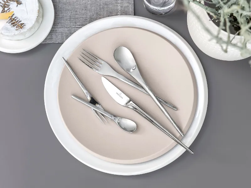 Des couverts de table NewMoon de Villeroy & Boch disposés sur une assiette beige placée sur un fond gris.