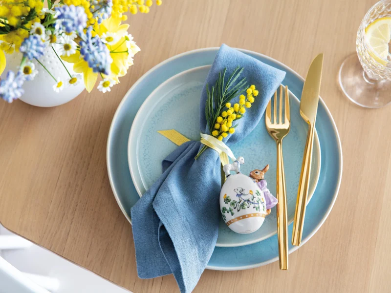 Une table élégamment dressée avec de la vaisselle Crafted bleue et un œuf décoratif de l’Annual Easter Edition 2022 ainsi qu’une composition florale printanière.