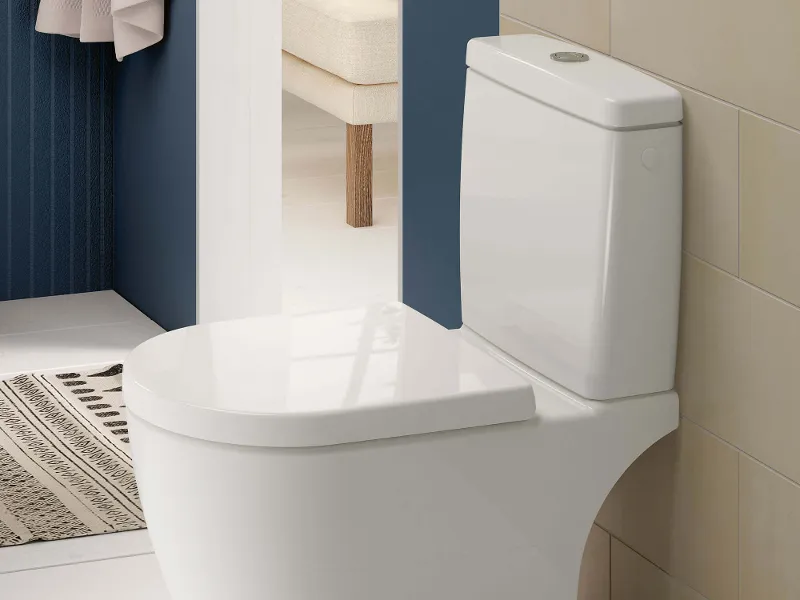 Un WC a colonna bianco con cassetta di risciacquo in un bagno pulito con pareti beige e blu