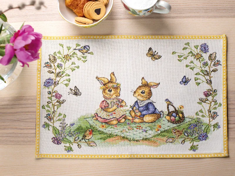 Spring Fantasy placemat with butterflies, flowers and birds on a wooden table with snacks and a vase of flowers.