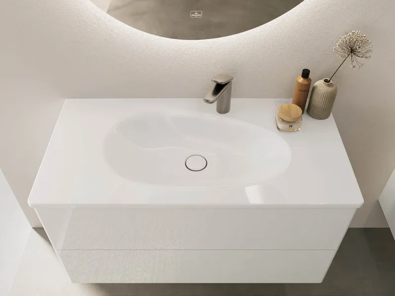 Un meuble sous plan avec un lavabo en blanc brillant ainsi qu’un miroir, de la décoration et un distributeur de savon Villeroy & Boch.