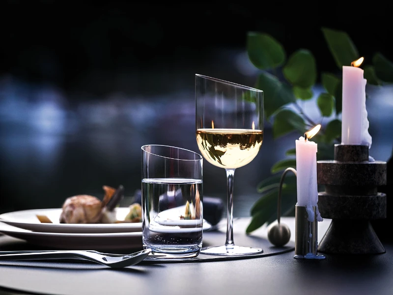 Des verres NewMoon contenant du vin et une bougie sur un ponton au crépuscule.