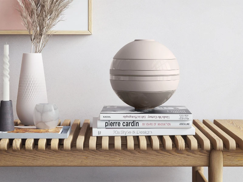 Eine beige La Boule von Villeroy & Boch auf einem Holztisch neben einer Vase und Büchern.