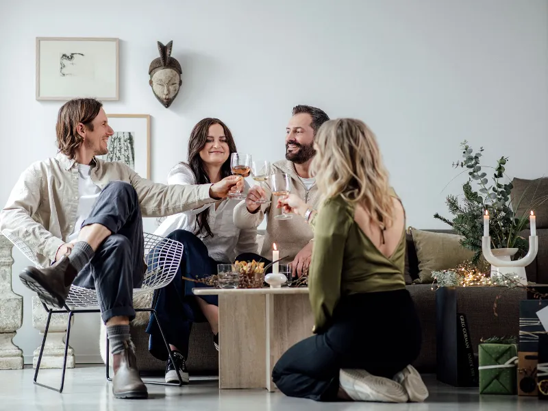 Vier personen proosten met Winter Glow glazen in een gezellige woonkamer versierd met kerstaccenten.