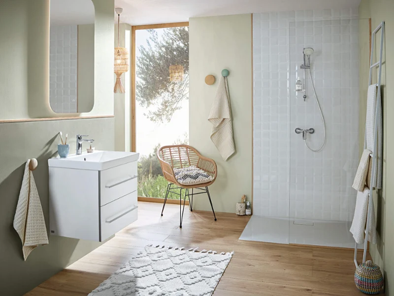 Salle de bain lumineuse avec parquet en bois clair, meuble-lavabo blanc et douche à l'italienne aux tons vert doux pour une ambiance fraîche et naturelle.