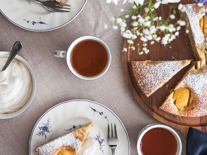 Stoviglie Vieux Luxembourg con pezzi di torta con panna montata, tè e fiori su un tavolo.