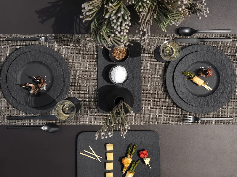 A modern dining table with two place settings, each with Manufacture plates, flatware, napkins, appetizers, and glasses.