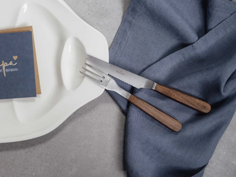 Une décoration de table élégante avec des couverts de table Texas modernes avec des manches en bois et un menu posé sur une serviette en lin texturé.