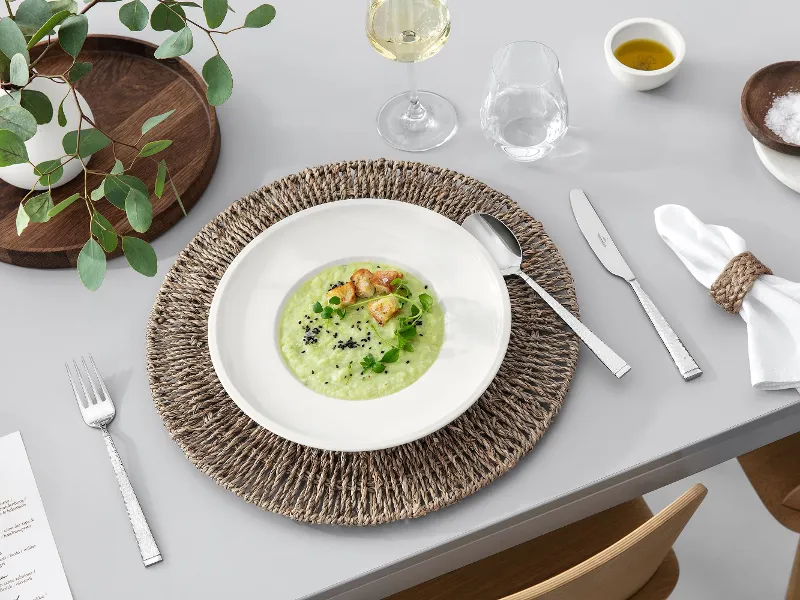 A dining table with Blacksmith flatware, an Artesano dish filled with soup, a glass of white wine and rustic table decorations.