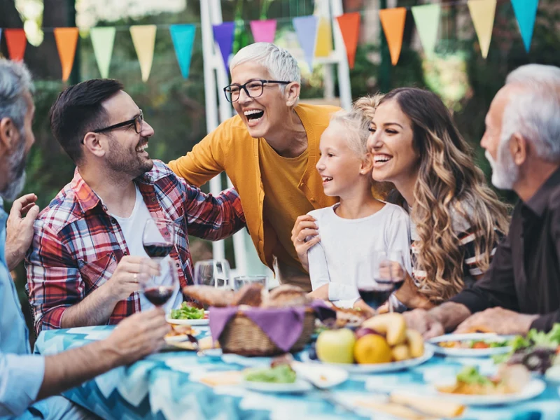 Six people are sitting around a table, laughing. Colorful pennants are decorating the background.