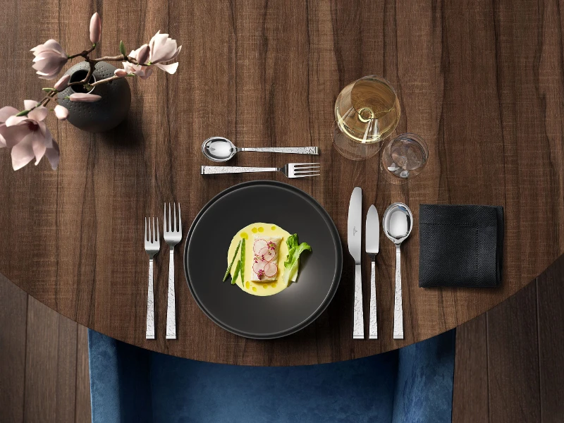 Elegantly set table with appetizer on a dark round table, accompanied by a glass of white wine and Blacksmith flatware set.