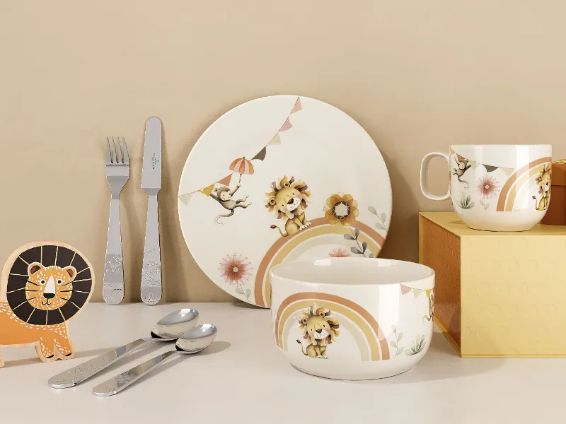 Das Tafelset „Boho Kids | Roar like a Lion“ von Villeroy & Boch besteht aus einem Teller, einer Schüssel, einem Becher, Besteck und einer Figur mit Löwenmotiv, präsentiert auf einer weißen Fläche mit beigem Hintergrund.