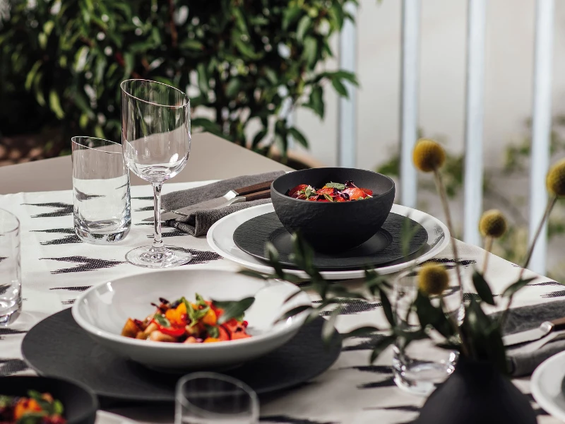 Une table dressée avec des assiettes et des plats creux noirs Manufacture et blancs NewMoon de Villeroy & Boch.