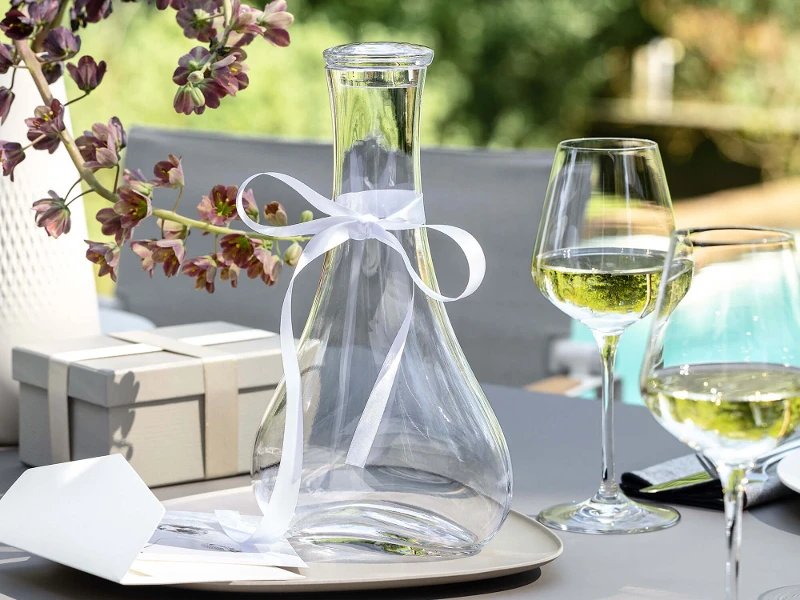 An elegant Purismo wine decanter with a white bow and wine glasses on a table.