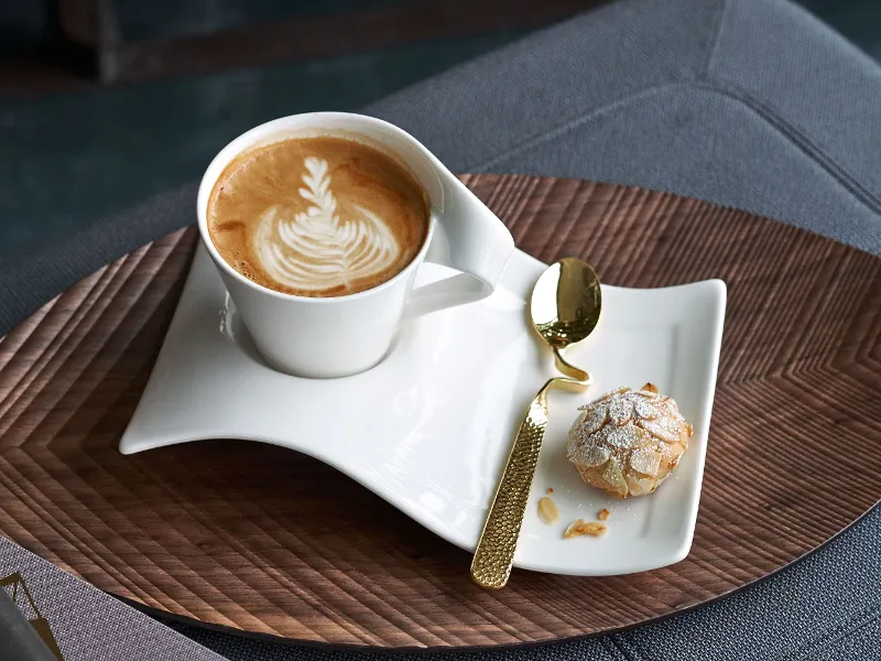 Une tasse NewWave avec du latte art et des biscuits sur une table en bois, accompagnés d’une cuillère NewWave raffinée.