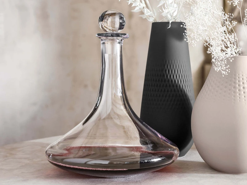 Une élégante carafe à vin Vinobile en verre et des vases Manufacture contenant des fleurs blanches.