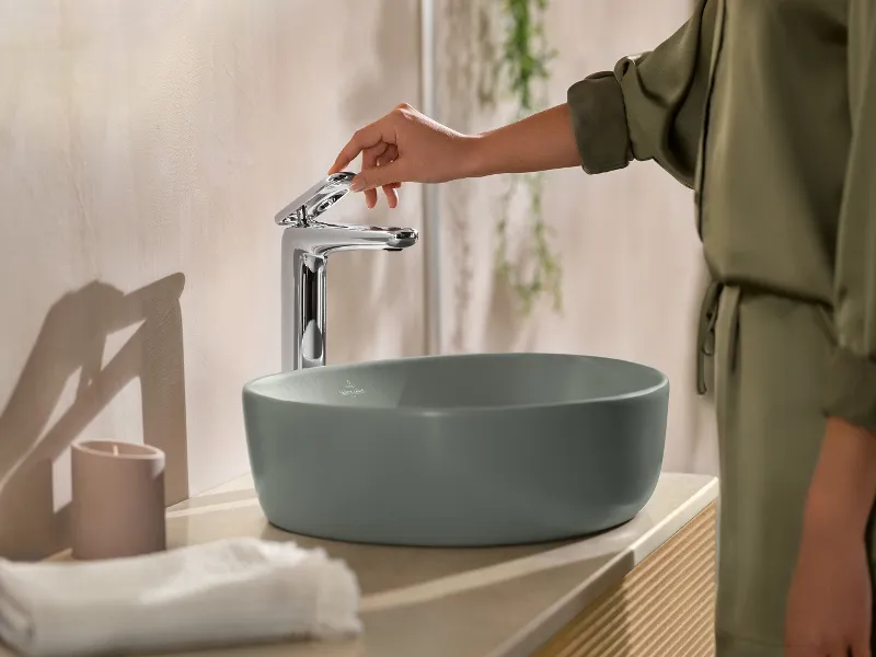 Une femme utilise un lavabo Antao Villeroy & Boch dans une salle de bains.