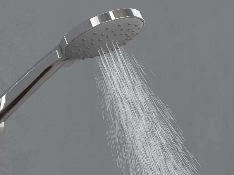Un rociador cromado que proyecta chorros de agua desde las boquillas centrales hacia abajo sobre un fondo gris sencillo.