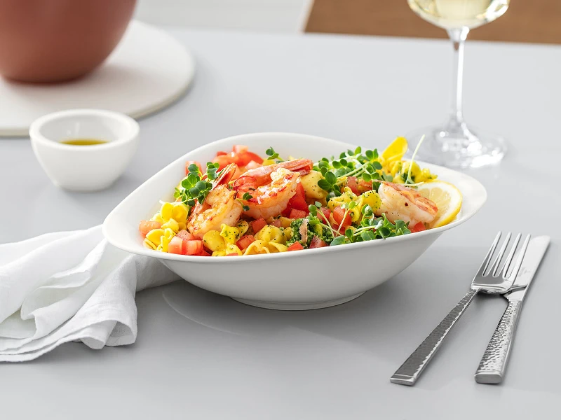 Villeroy & Boch Vapiano plate filled with a pasta salad on a wooden table. On the table there is a Villeroy & Boch wine glass and cutlery 