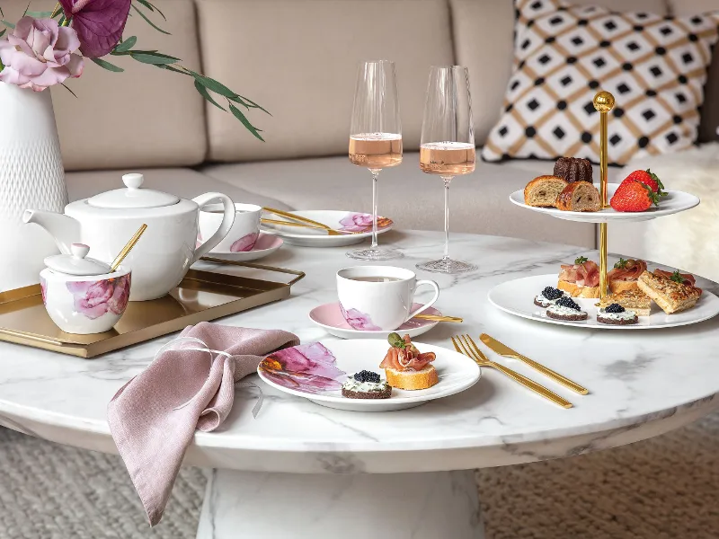 Une composition de table élégante pour le thé de l’après-midi avec des en-cas et du vin rosé sur une table en marbre, servis sur de la vaisselle Rose Garden de Villeroy & Boch.