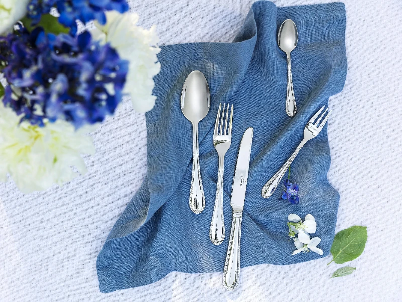 Une décoration de table élégante avec des couverts de table Mademoiselle sur une serviette en lin bleu et un bouquet de fleurs.