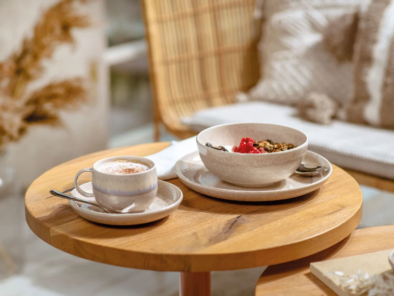 Een Perlemor kopje met koffie en een kom met muesli op een houten tafel.