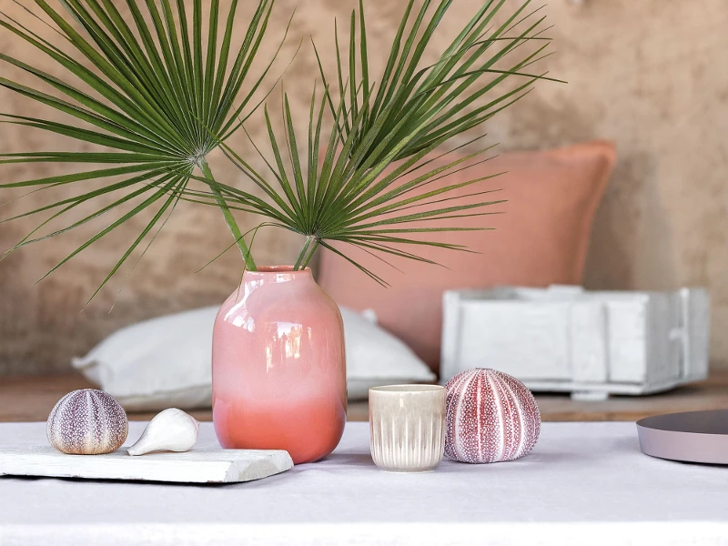 A table with a Perlemor vase and scented candle from like. by Villeroy & Boch with shells on it.