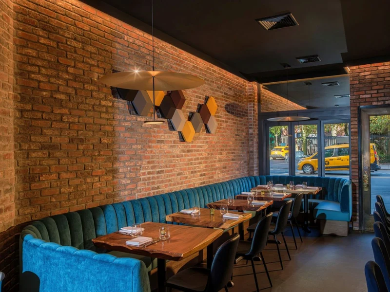 Inside of Arvine Restaurant Warm, modern restaurant interior with exposed brick, teal banquettes, wood tables, pendant lighting, geometric art, and a yellow taxi outside.