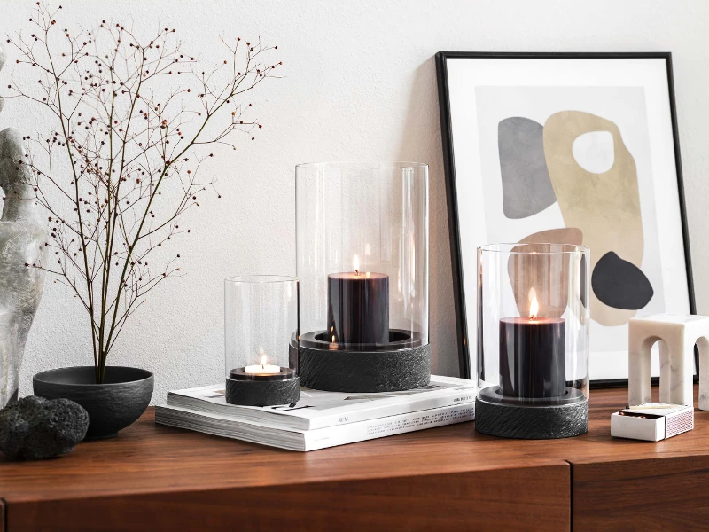 A modern home interior with a wooden sideboard and dried flower with three Manufacture hurricane lamps.