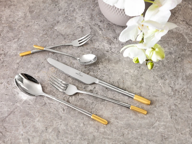 Elegant Ella flatware set with golden accents on a marble tabletop, accompanied by a white orchid.