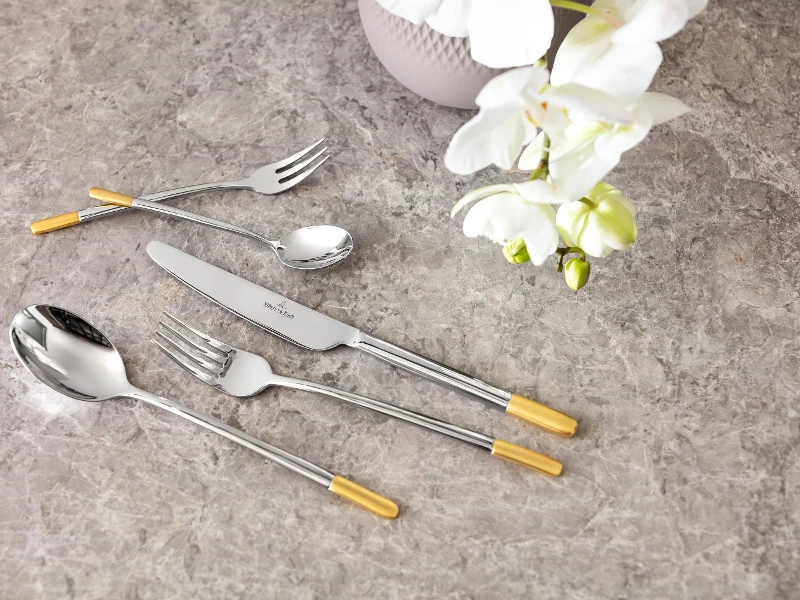 Ella flatware with gold-colored handles, arranged on a marble surface next to a white orchid.