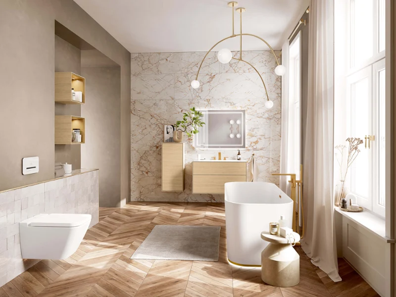 Freistehende weiße Badewanne mit goldfarbenen Mettlach-Armaturen in modernem Badezimmer mit Holzparkett und Marmorwand.