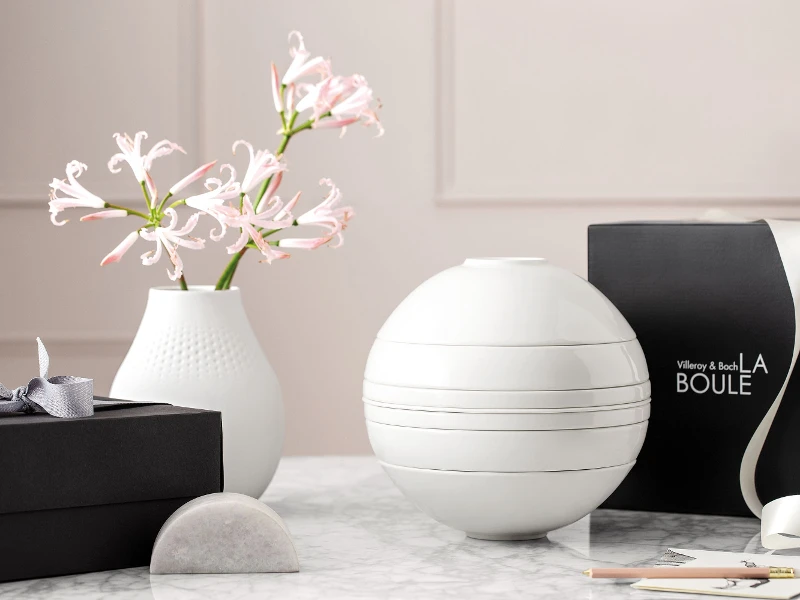 A white La Boule dinnerware set on a table with a black gift box behind it.