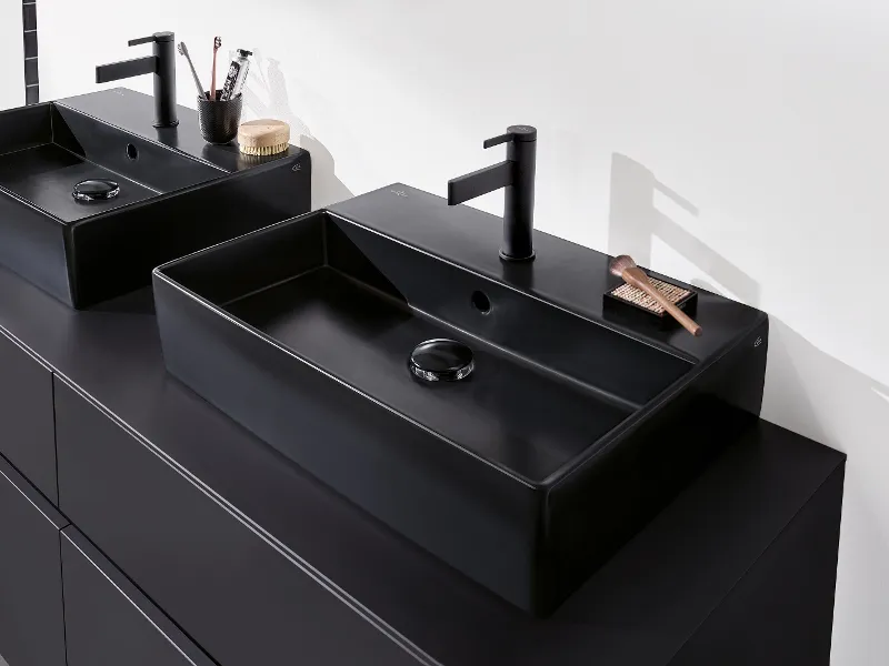 Zwei schwarze rechteckige Badezimmerwaschbecken von Villeroy & Boch mit mattschwarzen Wasserhähnen auf einer dunklen Arbeitsplatte, ausgestattet mit minimalistischen Badezimmerutensilien.