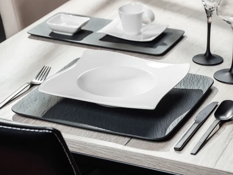 Modern table setting with Manufacture and NewMoon crockery and black Manufacture cutlery on a neutral tablecloth.