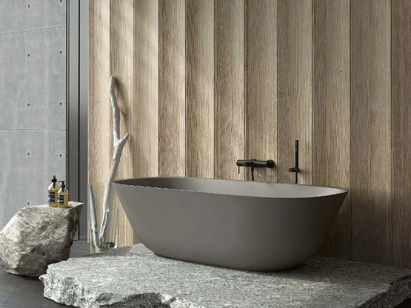 Bagno minimalista con vasca free-standing Theano grigia di Villeroy & Boch su una piattaforma in pietra.