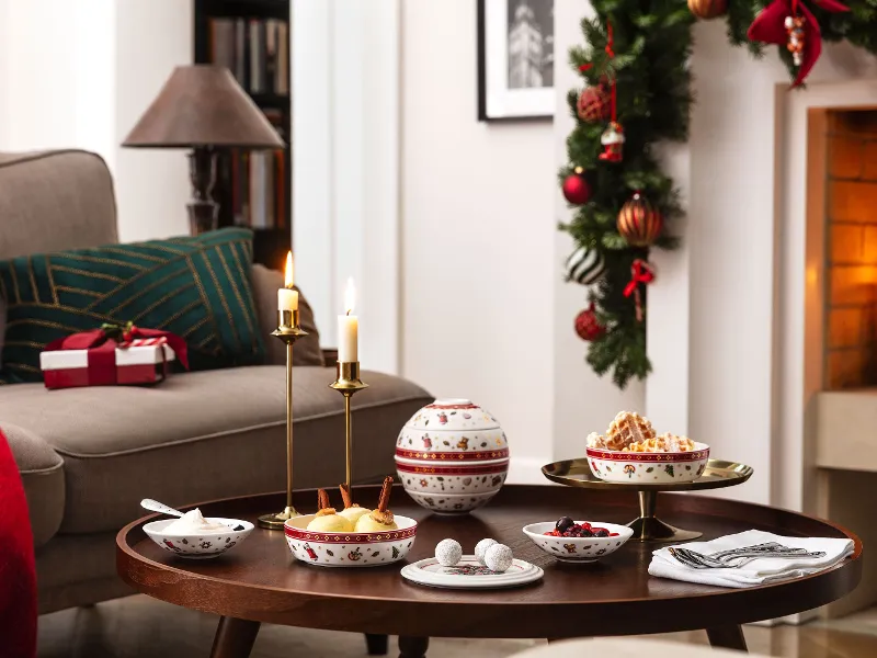 Une ambiance de salon festive avec un sapin de Noël décoré, une cheminée allumée et une table sur laquelle est dressée La petite Boule Toy's Delight