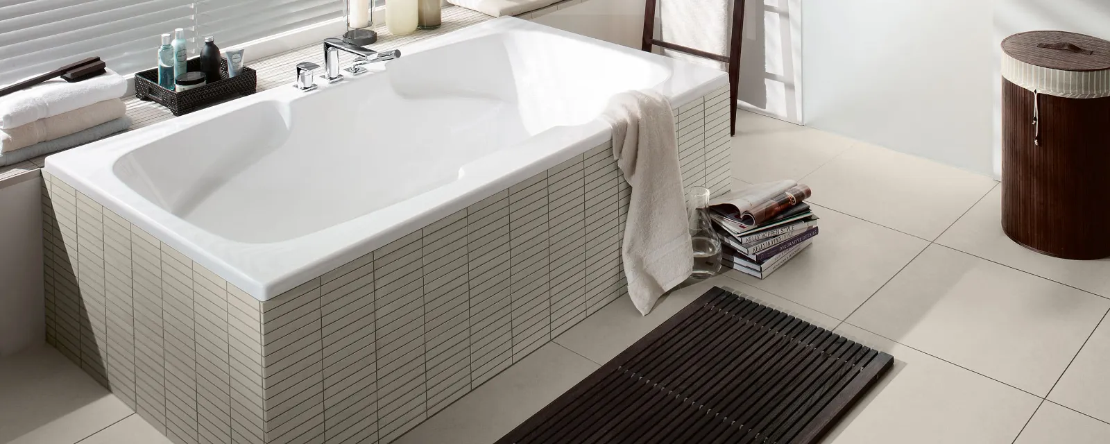 Eine weiße Colorado Badewanne in einem beigen Bad von Villeroy & Boch mit dekorierter Fensterbank.