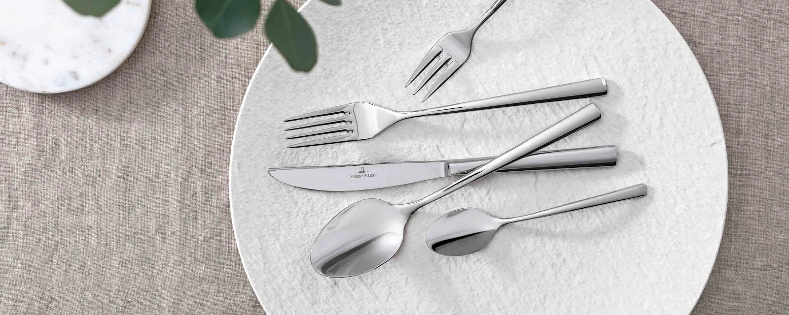 Elegant table decor with modern Piemont flatware and decorative green on a neutral table cloth.