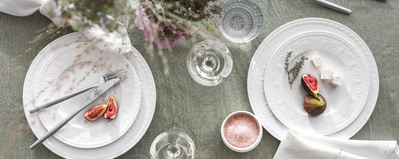 Villeroy & Boch Cellini plates with figs, cheese and herbs on a beautifully laid table. Glasses, cutlery, delicate flower arrangements and a bowl of salt on a green tablecloth add the finishing touches to the ambience.