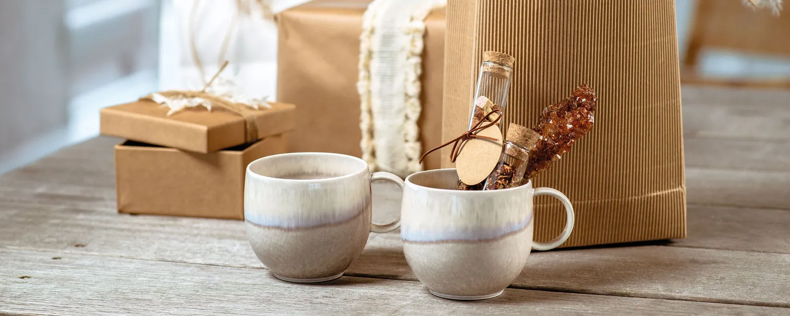 Brown gift boxes with a rustic aesthetic, in front of two ceramic mugs from the Perlemor collection by Villeroy & Boch on a wooden table.