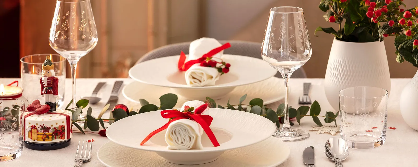 Elegant dining table setting for two people with white Manufacture plates Elegant dining table setting for two people with white Manufacture plates, napkins with red ribbons, wine glasses, silver cutlery and decorative plants.
