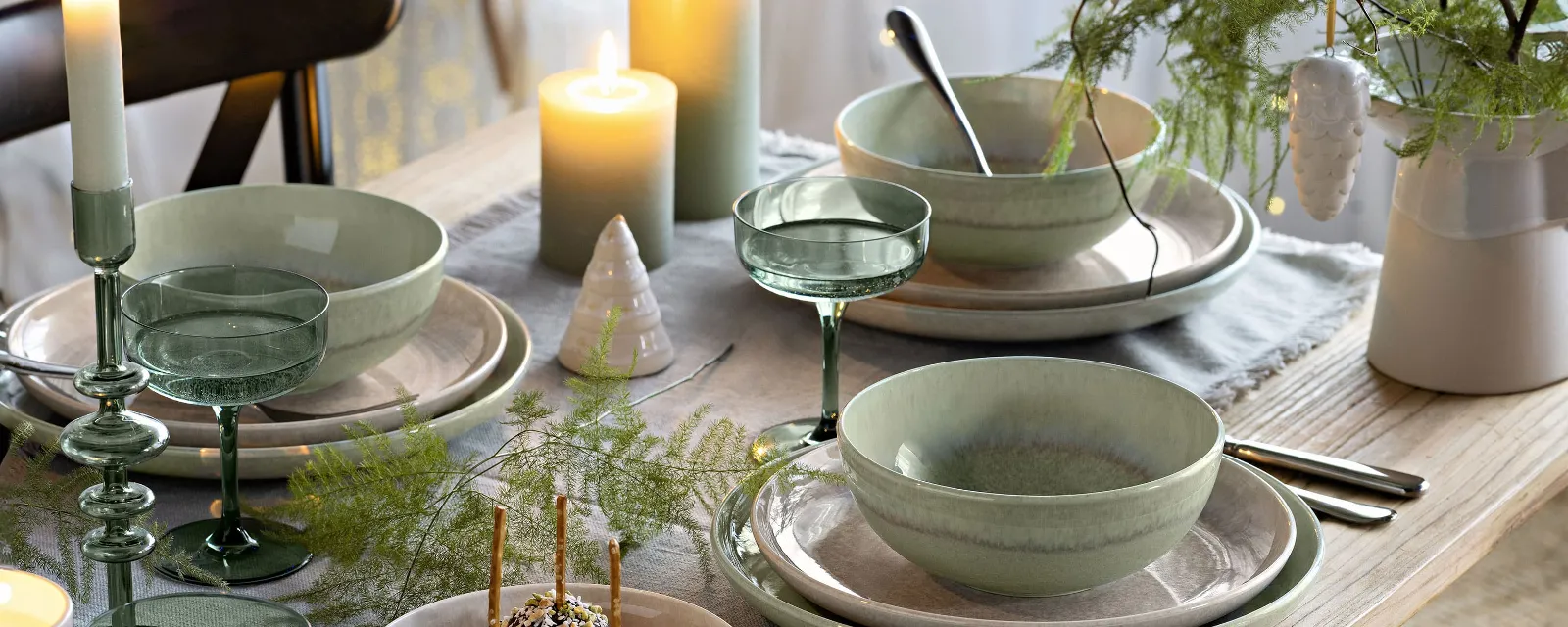 Festliche Tafel mit Perlemor Tellern und Winter Glow Dekorationen Festliche Tafel mit grünem und beigem Perlemor Tellern, umgeben von Winter Glow Kerzenhaltern und Like Gläsern.