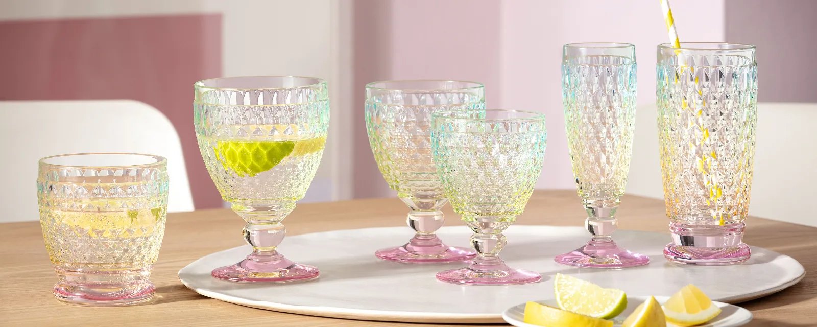 A set of six Villeroy & Boch Boston Pearl glass tumblers on a wooden table with lime and lemon slices, one tumbler with a straw and a lemon slice.