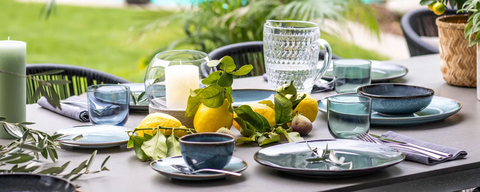 Eettafel buiten met Lave servies, glazen, kaarsen en verse citrusvruchten als middelpunt met uitzicht op een zwembad.