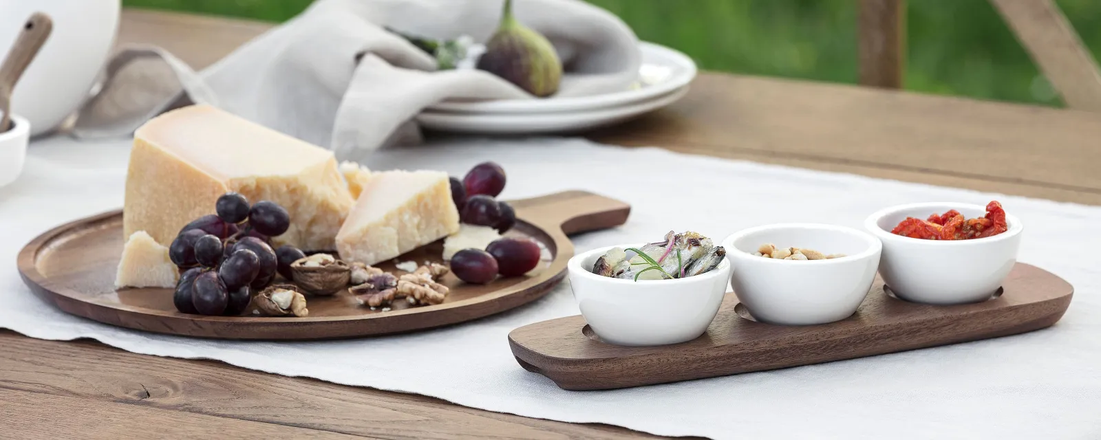 Villeroy & Boch Artesano wooden board, decorated with cheese, grapes, walnuts and figs. They are accompanied by three small dip bowls containing sliced vegetables, nuts and sun-dried tomatoes.