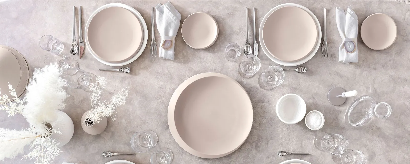 Et bord dekket med Villeroy & Boch NewMoon-tallerkener i beige og hvitt samt bestikk og glass.