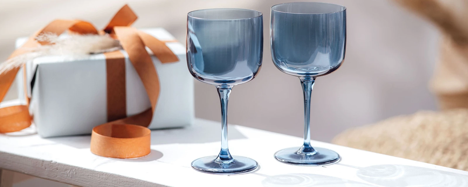 Deux verres à vin bleus like. sur une table à côté d’une boîte cadeau.