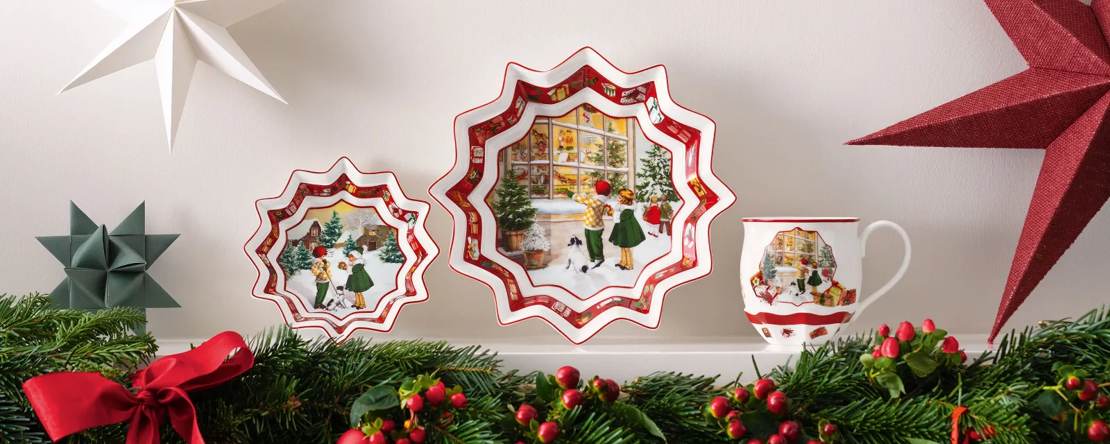 La collezione Toy's Fantasy di Villeroy & Boch, un piatto decorativo, una tazza decorata con paesaggi invernali, addobbi a forma di stella e una rigogliosa ghirlanda decorata con nastri rossi e bacche sulla mensola del camino.